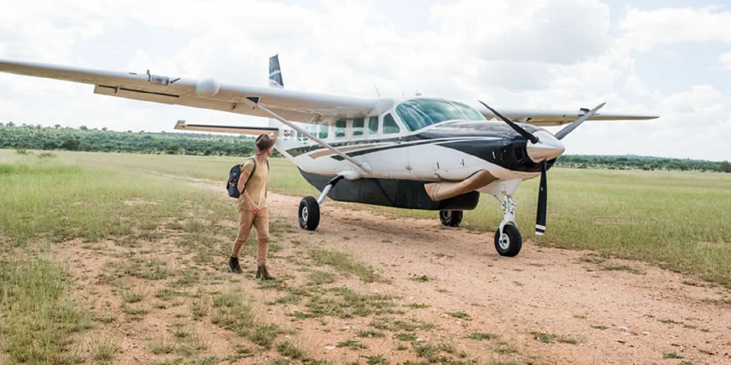 Piccolo aereo da bush Cessna Caravan parcheggiato su una pista di atterraggio in terra battuta nel mezzo di Amboseli, con elefanti visibili in lontananza e il Kilimanjaro sullo sfondo
