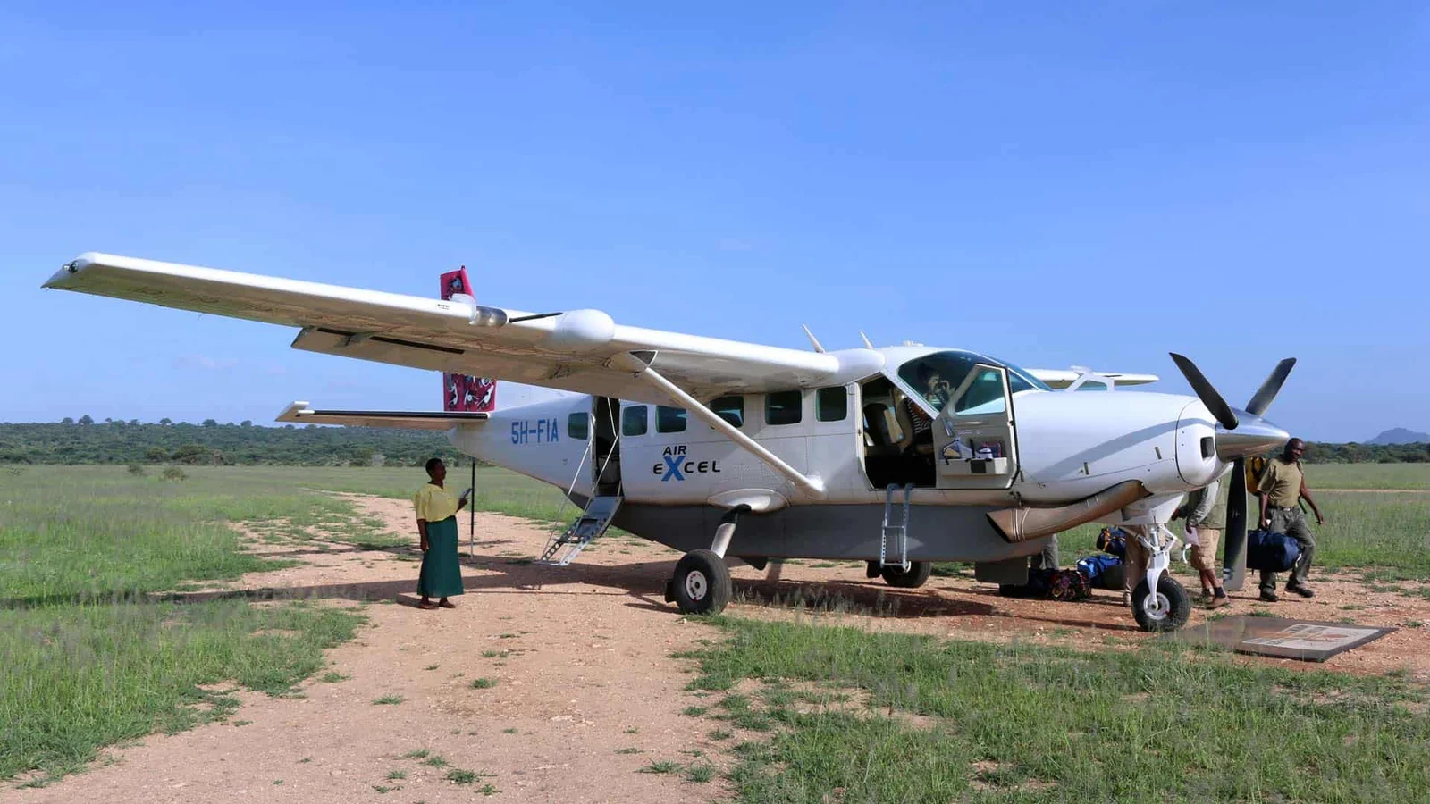 Cessna-Caravan-Buschflugzeug auf der Graspiste des Ikuu Airstrip mit wartenden Safarifahrzeugen neben der Landebahn