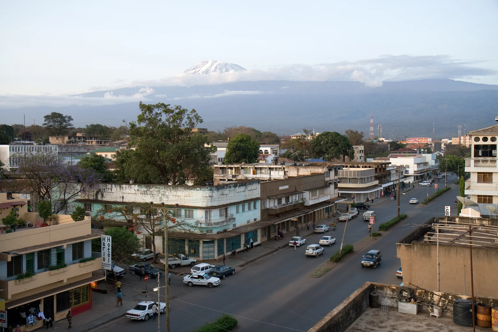 Escena callejera en la ciudad de Moshi con la cumbre nevada del Kilimanjaro visible más allá de los tejados en la luz de la mañana