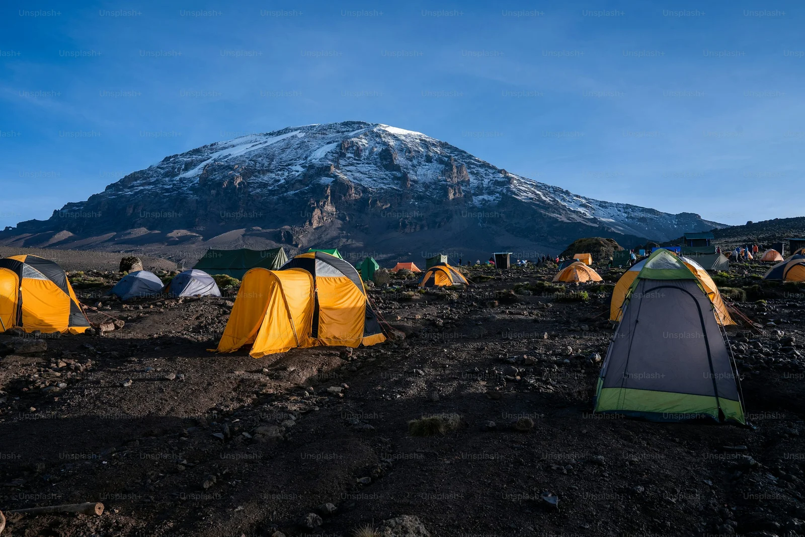 Camp sous tente au camp d'altitude de Barafu, avec du matériel de trekking séchant au soleil et le sommet de Kibo visible au-dessus