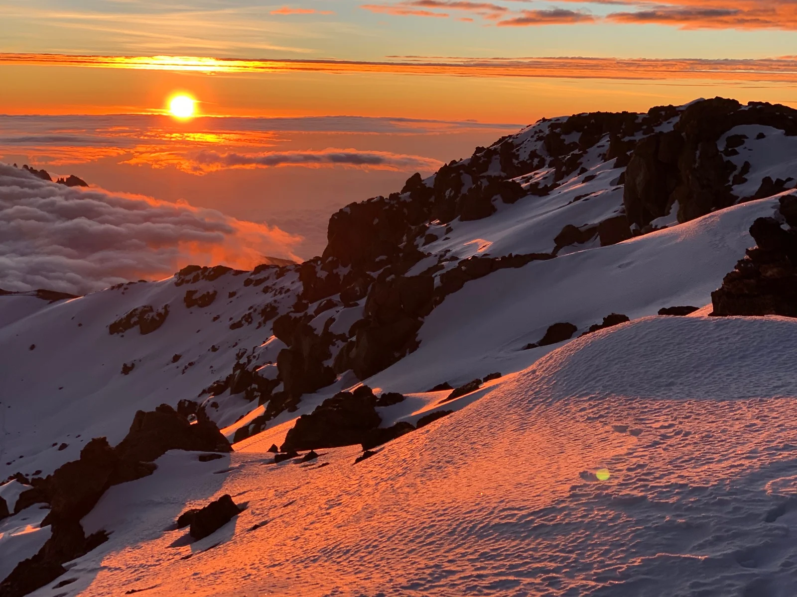 Amanecer desde la cresta de la cumbre del Kilimanjaro en Stella Point, con glaciares remanentes brillando en azul y blanco y nubes extendiéndose sobre las llanuras africanas abajo