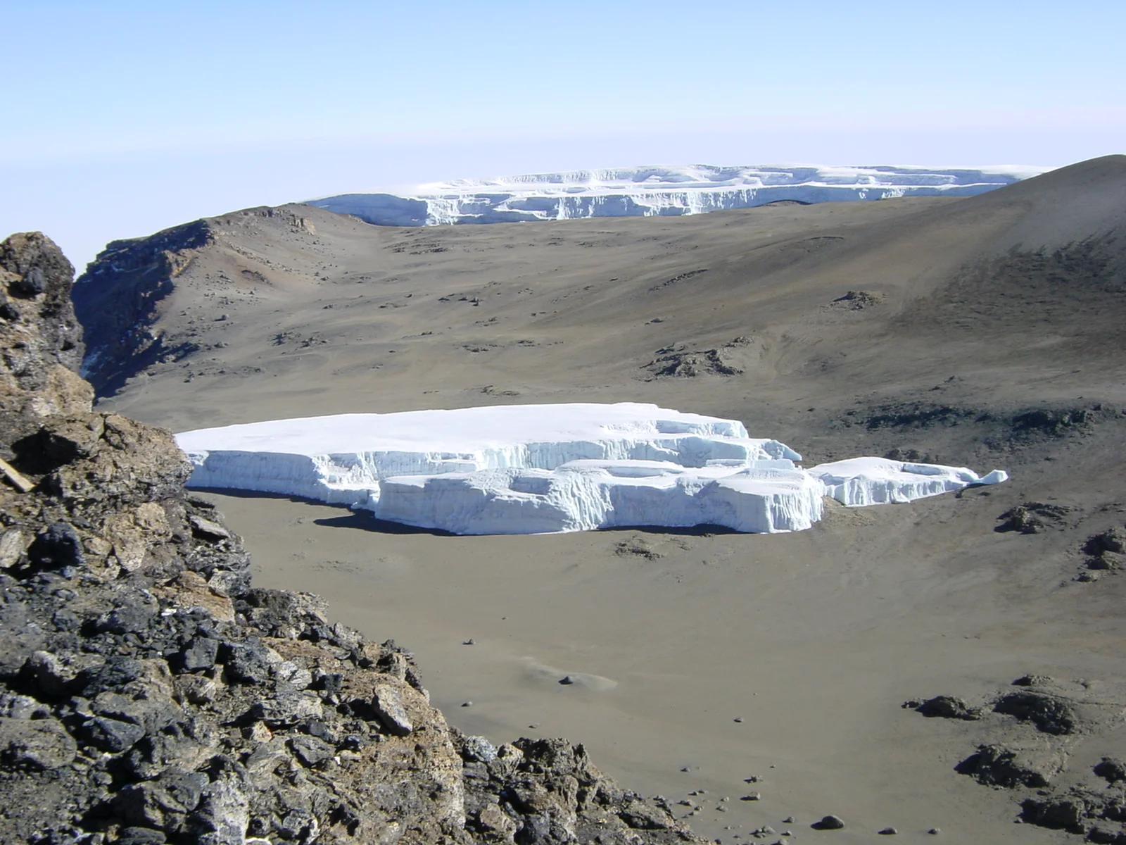 Muraille de glacier résiduelle près d'Uhuru Peak, avec une glace d'un blanc bleuté surplombant les éboulis volcaniques
