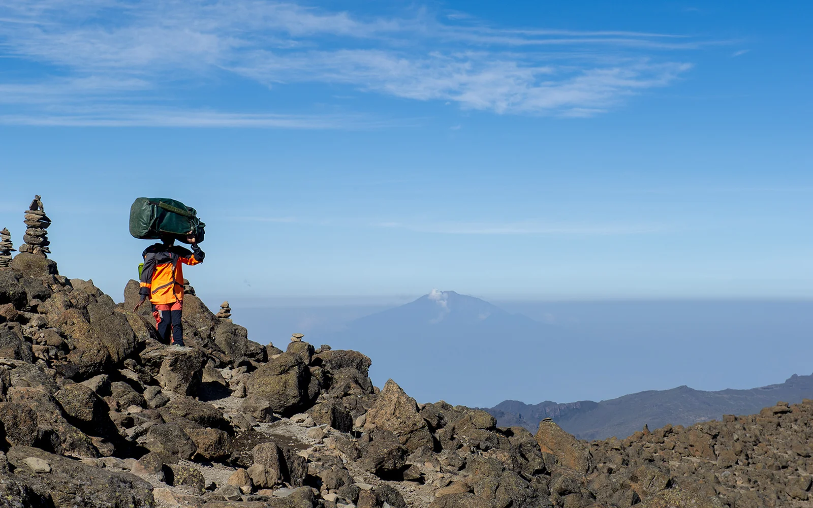 Un porteur du Kilimanjaro portant du matériel sur la tête, montant le sentier au-dessus de la limite des arbres