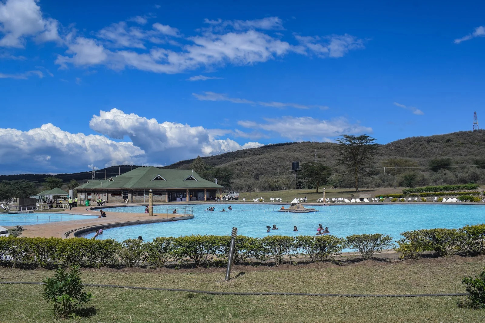 Ein Gast badet schwimmend im warmen dritten Becken des Olkaria Geothermal Spa, mit den Dampfsäulen der geothermischen Bohrlochköpfe in der Ferne sichtbar