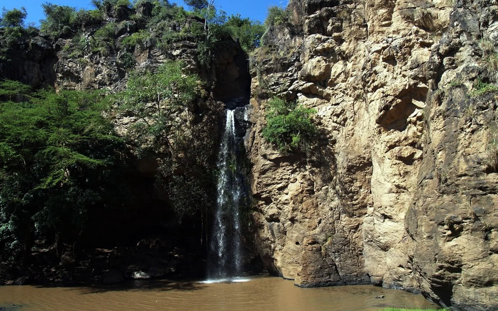 Die Makalia-Wasserfälle im südlichen Parkteil an einem Nachmittag in der grünen Saison — bescheiden im Ausmaß, aber in echtem Spitzmaulnashorn-Gebiet, und den halben Tag von den östlichen Lodges aus wert.