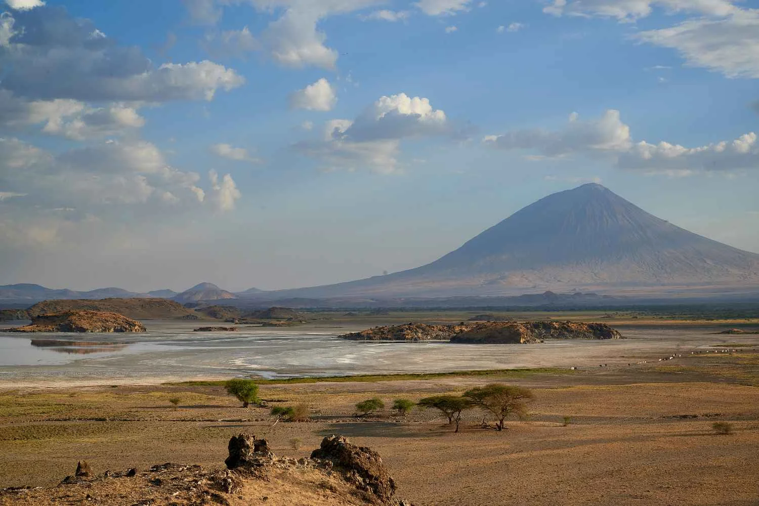Vue aérienne des eaux alcalines rouges du lac Natron s'étirant vers le cône parfait du volcan Ol Doinyo Lengai au lever du soleil