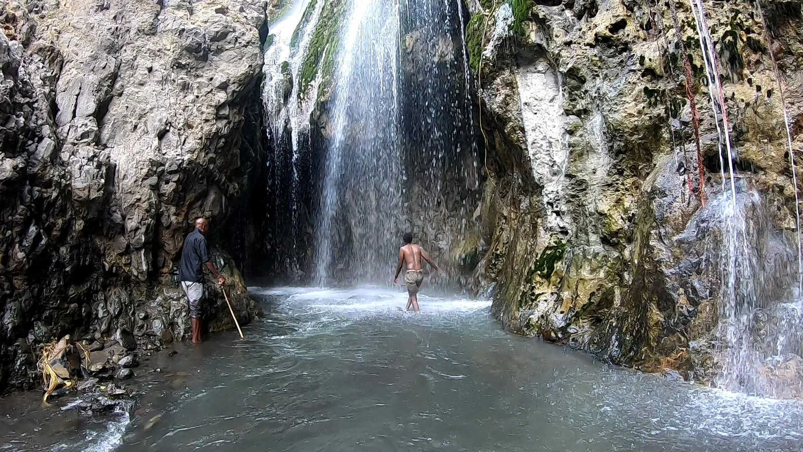 Baignade dans le bassin frais de la gorge sous la cascade d'Engare Sero, avec des falaises rouges au-dessus