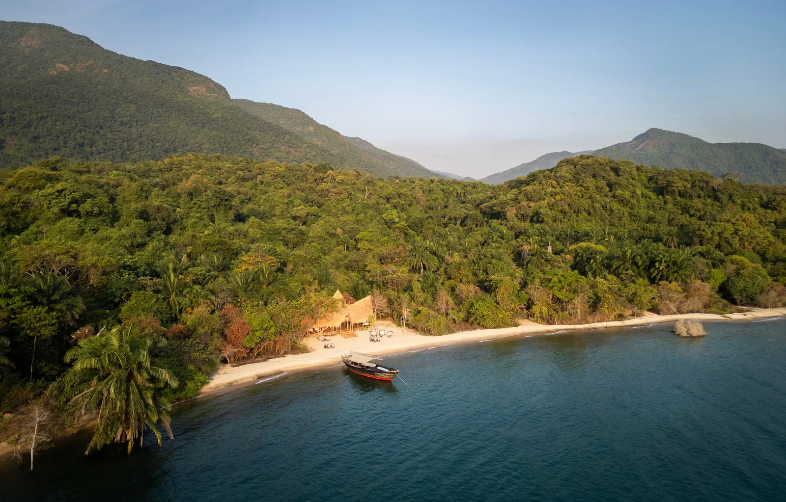 Kayak le long du rivage boisé de Mahale à l'aube, avec les montagnes se reflétant dans une eau immobile