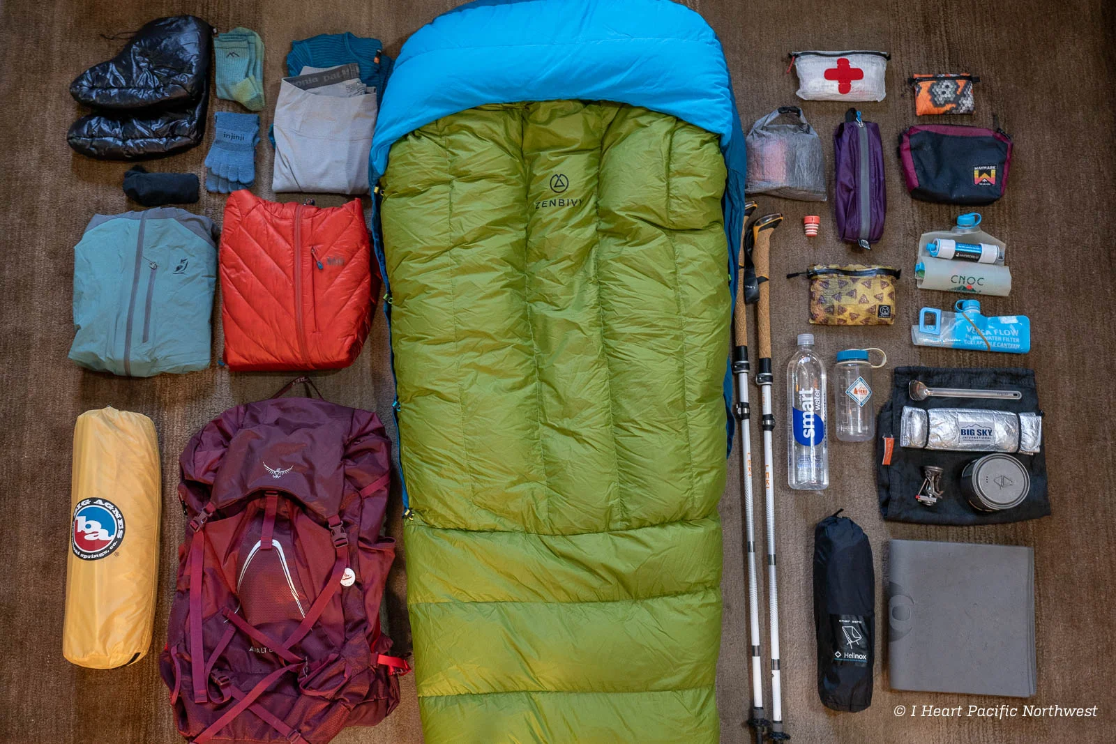 Équipement d'un grimpeur étalé sur un lit d'hôtel avant un briefing pour le Kilimanjaro — doudoune, sac de couchage, guêtres, chaussures, système de gants, lampe frontale, poche à eau