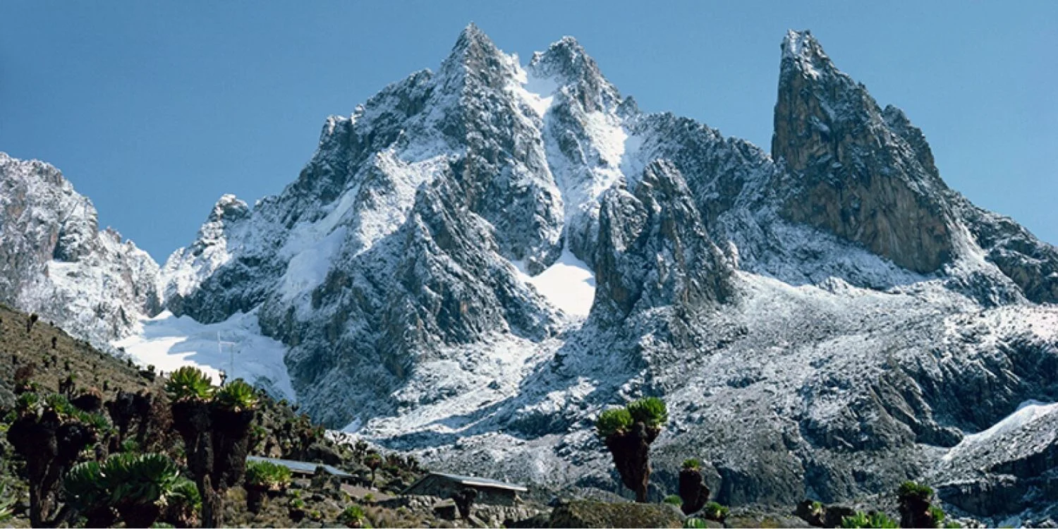 Schroffes Morgenlicht auf den Zwillingsgipfeln Batian und Nelion, gesehen von Point Lenana aus, mit Kletterern als Silhouette auf dem Grat