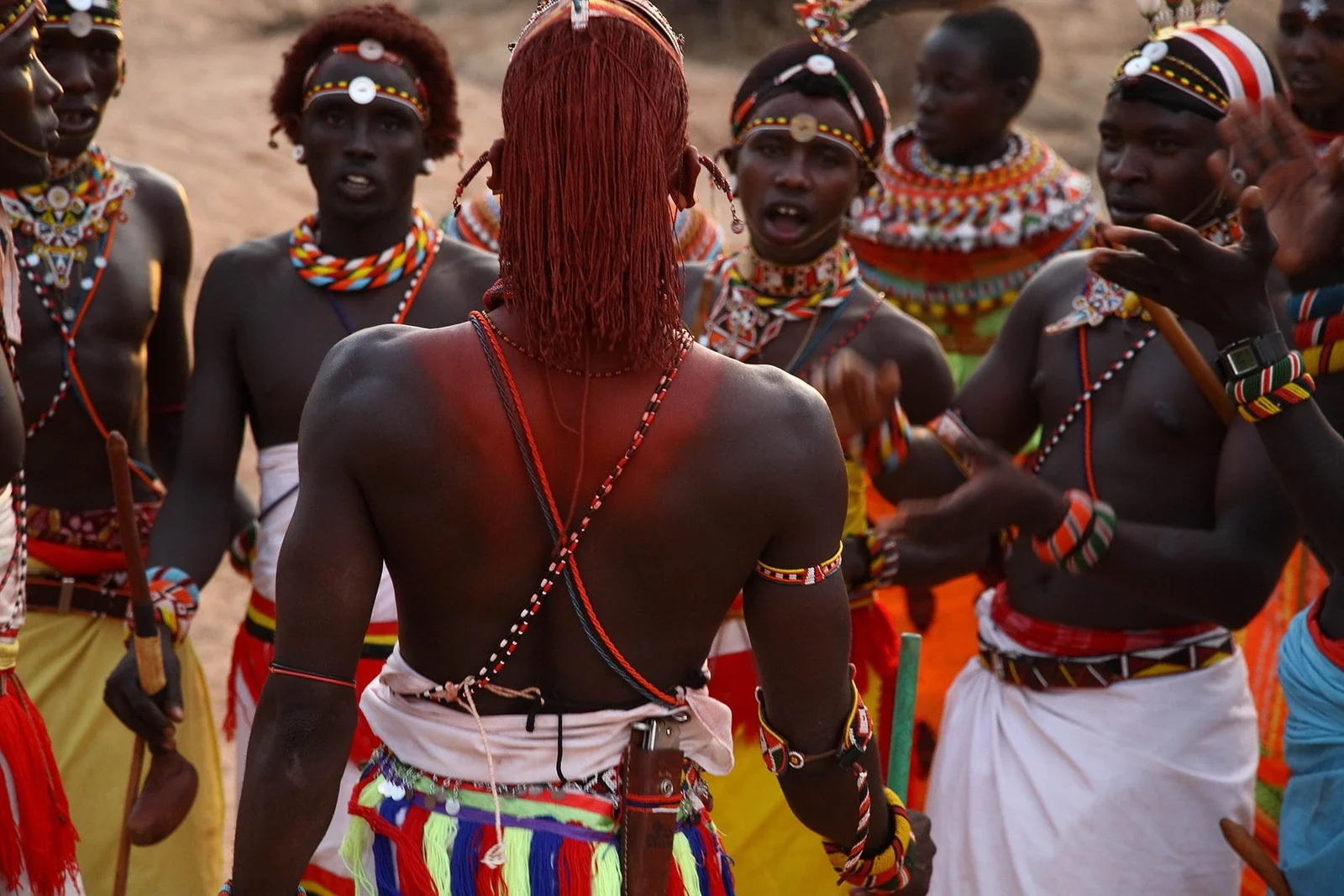 Ein Samburu-Krieger in traditionellem rotem Shuka-Gewand und Perlenschmuck steht auf einem Felsvorsprung, im Hintergrund die Mathews Range
