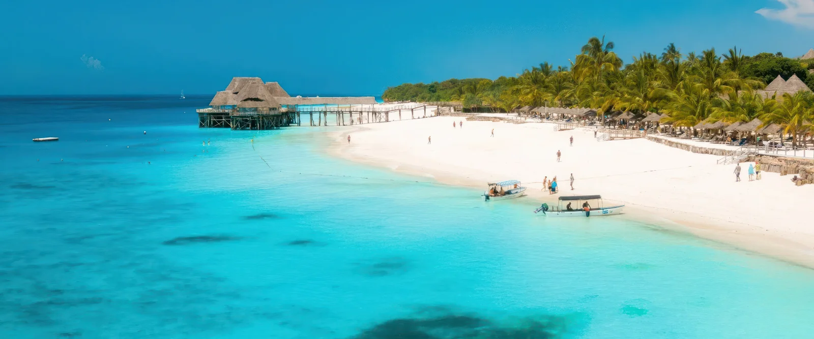 Agua turquesa del océano Índico encontrándose con arena blanca de coral en la playa de Nungwi, con dhows tradicionales de madera anclados en aguas poco profundas