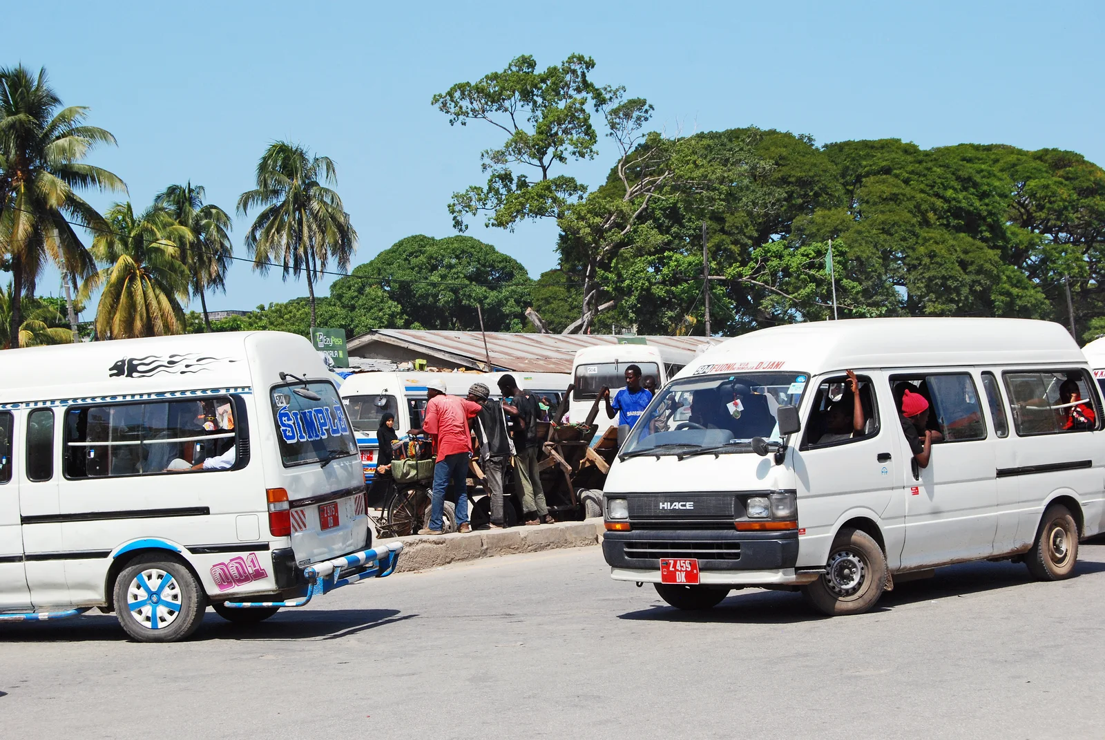 Carretera pavimentada a través de un pueblo de Zanzibar con palmeras a ambos lados y un minibús dala dala compartido transportando pasajeros