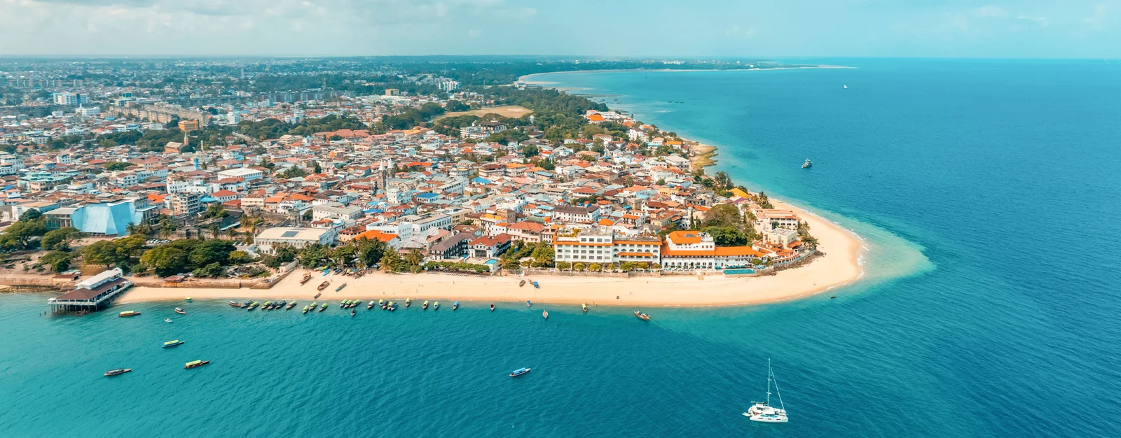 Vista aérea de los tejados de piedra coralina y los estrechos callejones de Stone Town encontrándose con el paseo marítimo del Océano Índico al atardecer
